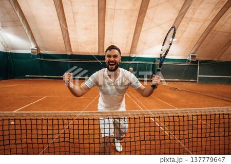 Very happy, smiling, cheerful. Man is playing tennis indoors in the hangar Very happy, smiling, cheerful. Man is playing tennis indoors in the hangar 137779647