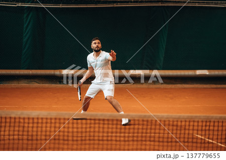 Front view. Man is playing tennis indoors in the hangar Front view. Man is playing tennis indoors in the hangar 137779655