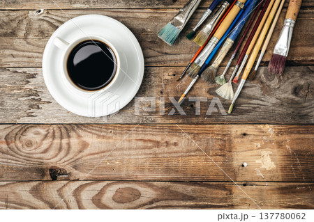 Paint brushes and a cup of coffee on a wooden background, flat lay. Paint brushes and a cup of coffee on a wooden background, flat lay. 137780062