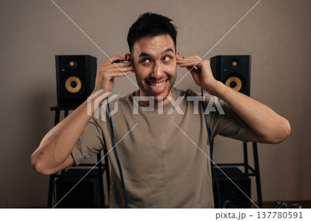 Portrait of cheerful male sound engineer making playful face listening through in ear monitors and adjusting audio in a professional recording studio, focused and cheerful during music production. 137780591