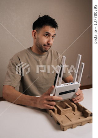 Vertical shot of technician holding new white wireless router, studying setup and placement for optimal home wifi performance and stable internet connection in modern living space, casual tech review. 137780595