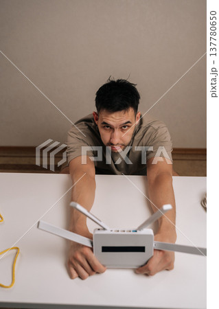 Vertical portrait of technician holding white wireless internet router with multiple antennas, looking at camera while setting up the device for improved home network and high speed online access. Vertical portrait of technician holding white wireless internet router with multiple antennas, looking at camera while setting up the device for improved home network and high speed online access. 137780650