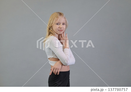 A blonde girl in a white crop top and black pants stands with her hand near her face, showcasing a mix of youthful fashion and thoughtful poise. The scene emphasizes contemporary fashion and serene A blonde girl in a white crop top and black pants stands with her hand near her face, showcasing a mix of youthful fashion and thoughtful poise. The scene emphasizes contemporary fashion and serene 137780757