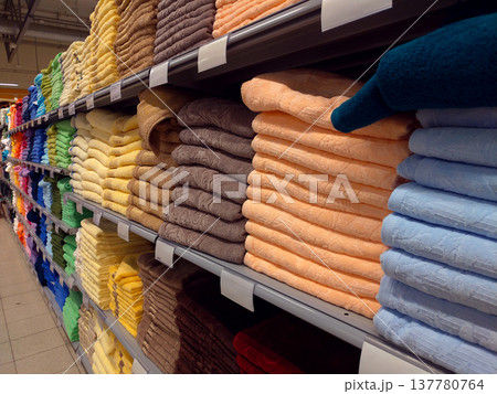 Rows of folded colorful towels arranged in a store aisle selling home textiles. The retail scene illustrates interior goods, household products and shopping environment. Rows of folded colorful towels arranged in a store aisle selling home textiles. The retail scene illustrates interior goods, household products and shopping environment. 137780764