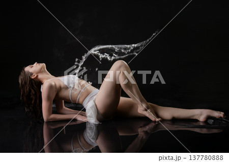 Elegant woman in white lingerie lying on a black reflective floor with a dramatic water splash in motion. Elegant woman in white lingerie lying on a black reflective floor with a dramatic water splash in motion. 137780888
