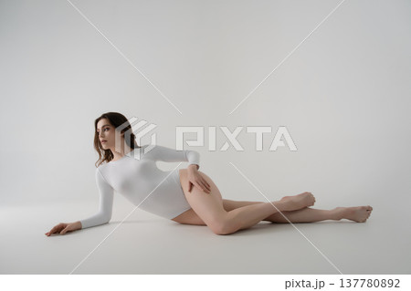 Elegant woman in a white bodysuit lying gracefully on a minimalist studio background with copy space. Elegant woman in a white bodysuit lying gracefully on a minimalist studio background with copy space. 137780892