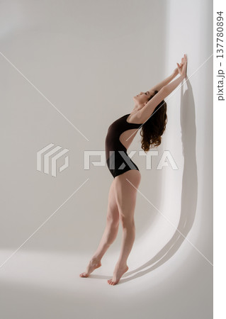 Elegant female dancer in leotard arching back in a minimalist studio. 137780894