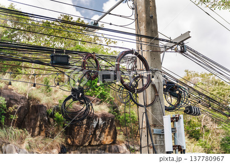 Messy overhead utility cables and telecom wires on concrete pole in tropical Thailand 137780967