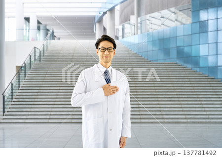 病院のロビーに立つ誠実な若い男性医師(胸に手を当てる) 病院のロビーに立つ誠実な若い男性医師(胸に手を当てる) 137781492