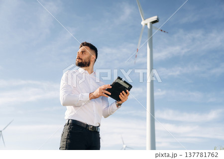 Digital tablet in hands. Engineer in field checking on wind turbine production Digital tablet in hands. Engineer in field checking on wind turbine production 137781762