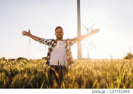Hands to the sides, happy. Guy engineer in wheat field against wind turbines 137781804