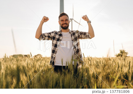 Beautiful nature. Guy engineer in wheat field against wind turbines Beautiful nature. Guy engineer in wheat field against wind turbines 137781806