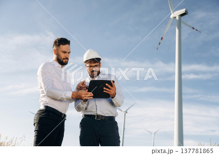 Getting to know the plan. Two men engineers are on field, with wind turbines Getting to know the plan. Two men engineers are on field, with wind turbines 137781865