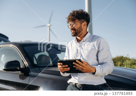 By the front of the car, with tablet. Male engineer in field checking on wind turbine production 137781893