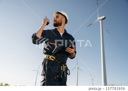 Giving orders by using walkie talkie. Engineer in field checking on wind turbine production 137781939