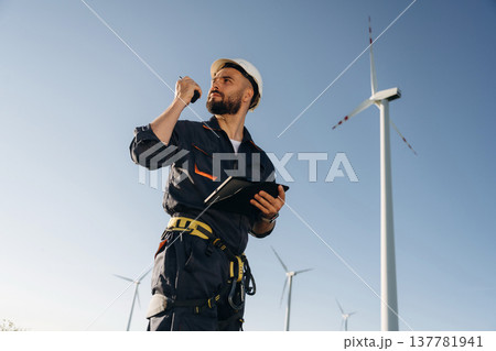 Communicating by walkie talkie. Engineer in field checking on wind turbine production Communicating by walkie talkie. Engineer in field checking on wind turbine production 137781941