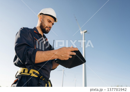 Reading information on digital tablet. Engineer in field checking on wind turbine production Reading information on digital tablet. Engineer in field checking on wind turbine production 137781942