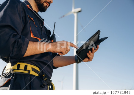 Detailed close up view of engineer in field with wind turbines against him Detailed close up view of engineer in field with wind turbines against him 137781945