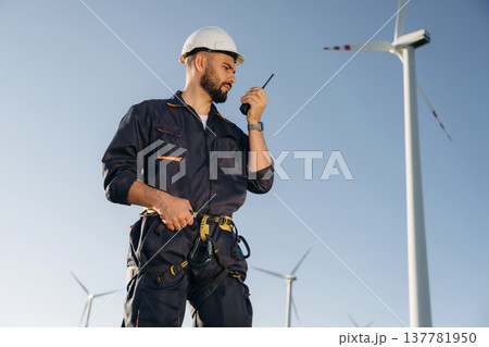 Communicating by walkie talkie. Engineer in field checking on wind turbine production Communicating by walkie talkie. Engineer in field checking on wind turbine production 137781950
