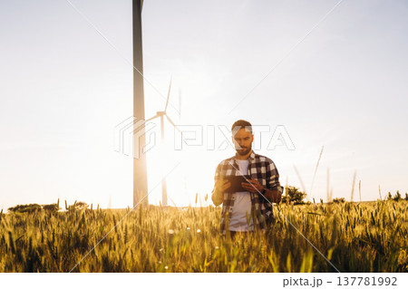 Sunny weather, front view. Guy engineer in wheat field against wind turbines 137781992