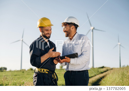 Cooperation concept. Two men engineers are on field, with wind turbines Cooperation concept. Two men engineers are on field, with wind turbines 137782005