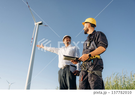 Making the business. Two men engineers are on field, with wind turbines Making the business. Two men engineers are on field, with wind turbines 137782010
