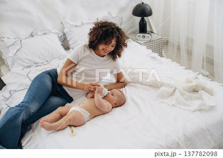 Feeding by using a bottle. Young woman is with her young baby daughter indoors Feeding by using a bottle. Young woman is with her young baby daughter indoors 137782098
