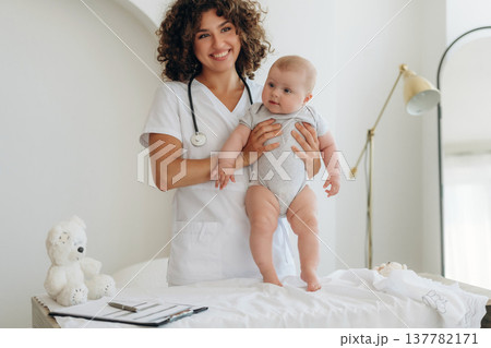 Smiling, holding baby in hands. Female doctor is with newborn indoors 137782171