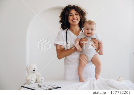 On the table and in hands, trying to stand up. Female doctor is with newborn baby indoors 137782202