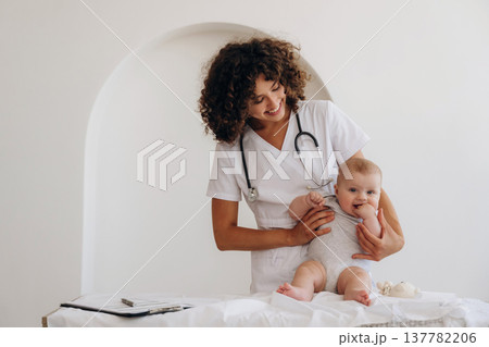 On the table and in hands, trying to stand up. Female doctor is with newborn baby indoors On the table and in hands, trying to stand up. Female doctor is with newborn baby indoors 137782206