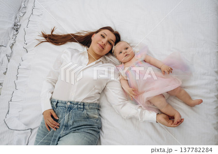 Top down view, lying down together. Happy mother is with her baby daughter indoors Top down view, lying down together. Happy mother is with her baby daughter indoors 137782284