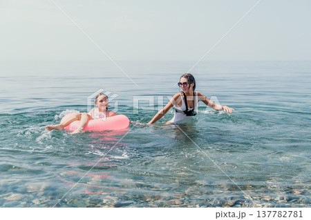 Family beach swimming mother and daughter enjoy swimming in the calm ocean with a pink inflatable ring during a happy summer vacation 137782781