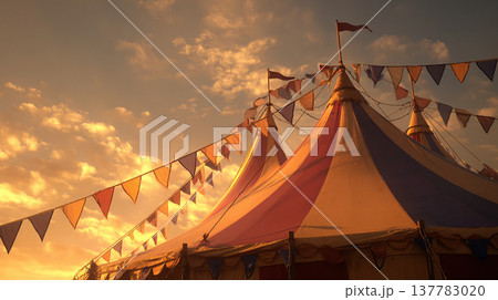 Colorful circus tent stands in the evening light with flags waving against a sunset sky Colorful circus tent stands in the evening light with flags waving against a sunset sky 137783020