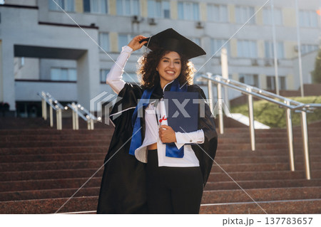 Cheerful graduate student in a gown is standing outdoors 137783657