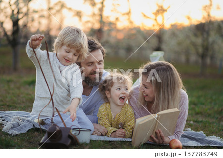 Family having picnic in spring nature, reading book on picnic blanket. 137783749