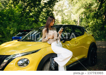 Leaning on the vehicle, using phone. Young woman is in the forest with two cars Leaning on the vehicle, using phone. Young woman is in the forest with two cars 137783993