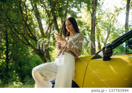 Smartphone is in hands. Woman is with her car in the forest Smartphone is in hands. Woman is with her car in the forest 137783994