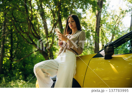 Smartphone is in hands. Woman is with her car in the forest 137783995