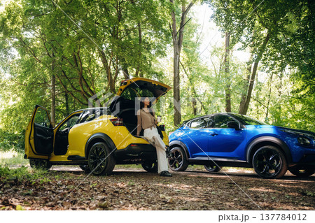 Vacation conception. Holding drink in hands. Young woman is in the forest with two cars 137784012