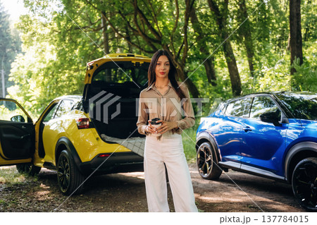 Young woman is in the forest with two cars Young woman is in the forest with two cars 137784015