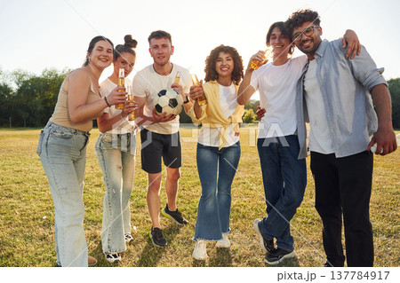 Quality drink, holding beer bottles and cheering. Young friends are having fun on the field Quality drink, holding beer bottles and cheering. Young friends are having fun on the field 137784917