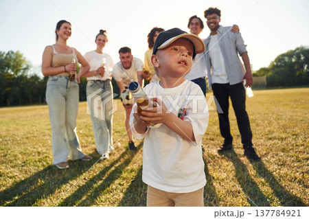 Little boy is standing and holding bottle. Young friends are having fun on the field 137784921