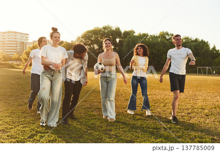 Under beautiful bright sunlight. Young friends are having fun on the field with soccer ball 137785009