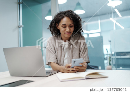 Female Professional At Her Desk Creating Social Media Update While Balancing Gadgets And Notes 137785041