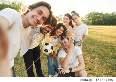 Handsome man is doing a selfie. Young friends are having fun on the field with soccer ball 137785160