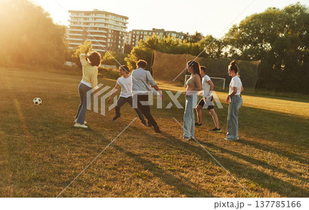 Under beautiful bright sunlight. Young friends are having fun on the field with soccer ball 137785166