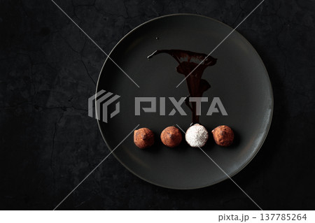 Chocolate truffles on a black plate. 137785264