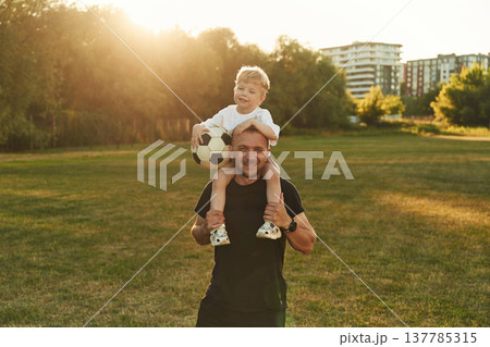 Soccer ball in hands. Father with his son are on the green field together Soccer ball in hands. Father with his son are on the green field together 137785315
