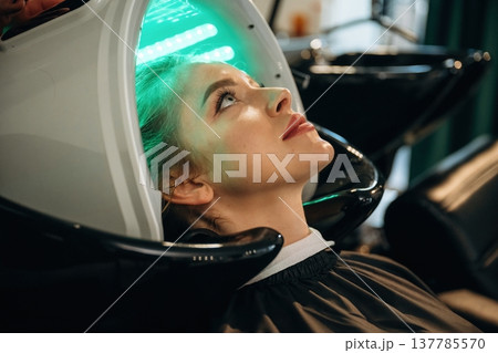 Green color. Woman is in a beauty salon with LED hair growth helmet 137785570