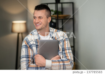Confident male holding laptop in home workspace 137785583